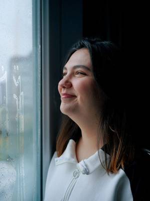 Frau schaut hoffnungsvoll lächelnd aus einem Fenster
